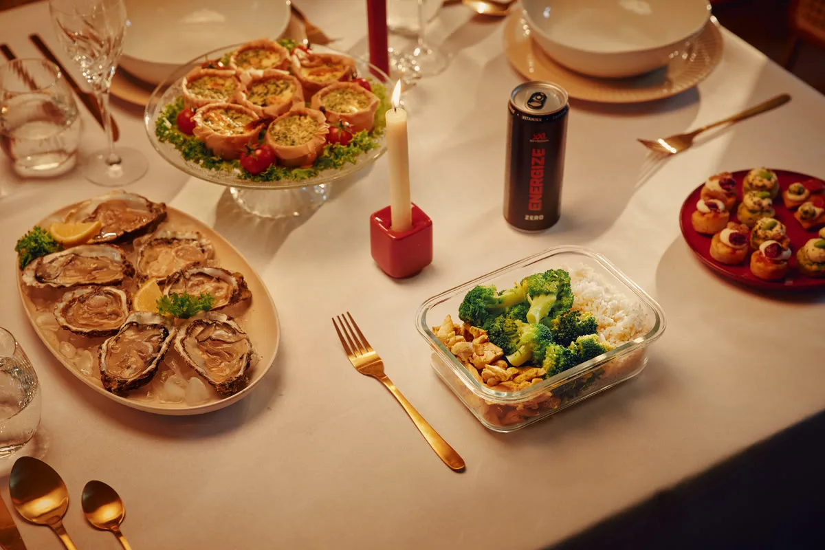 Een feestelijk gedekte kersttafel met een bakje kip, rijst en broccoli tussen de schalen