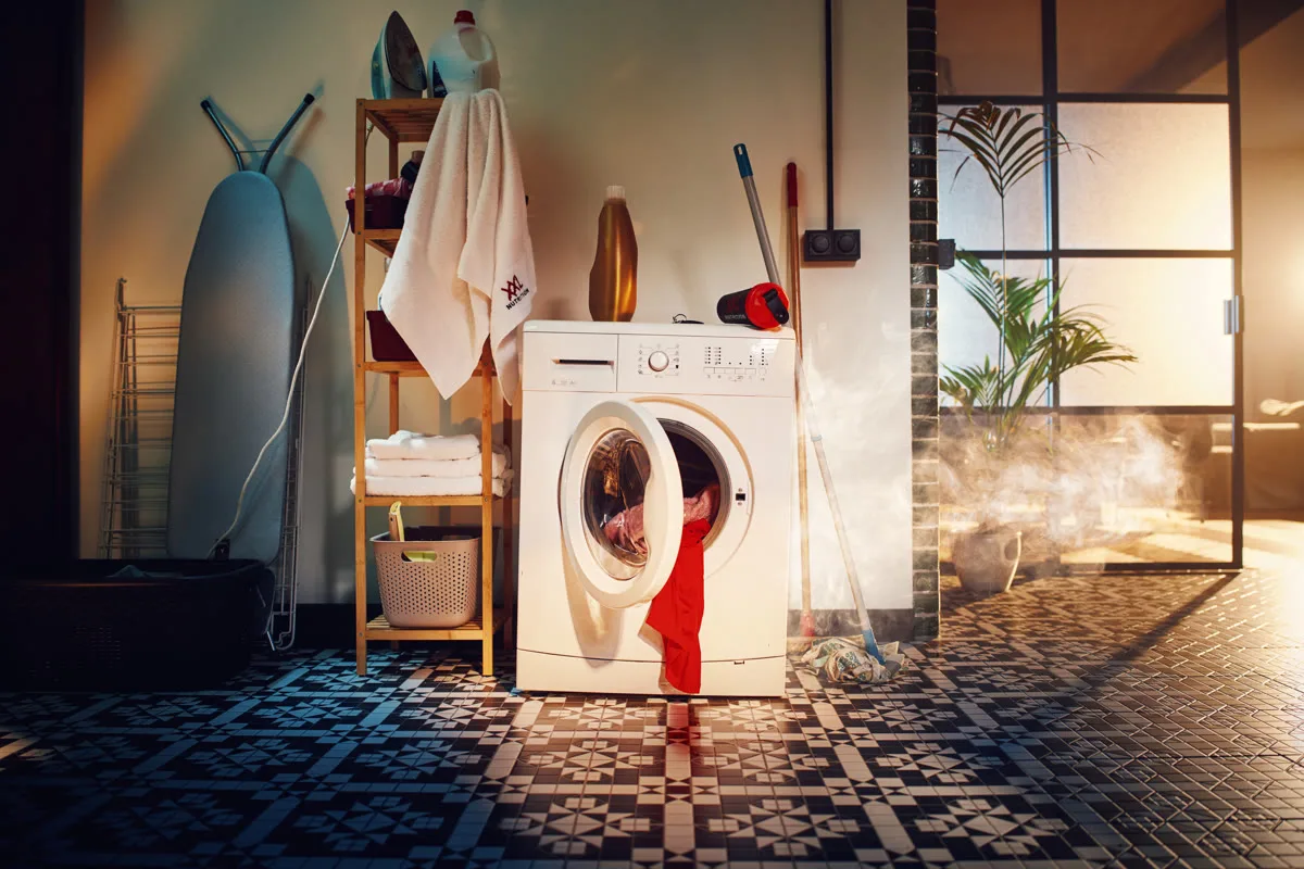 Een wasmachine met de deur open waaruit rode sportkleding hangt, in een badkamer met patroontegels